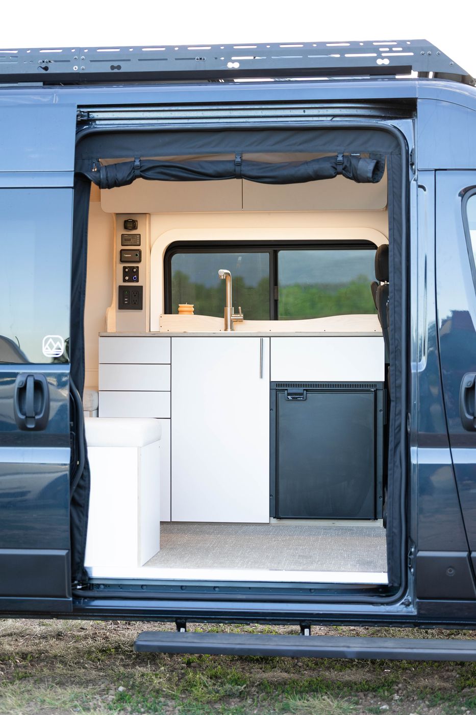 The sliding door of a DM Vans camper van open, looking into the galley and fridge