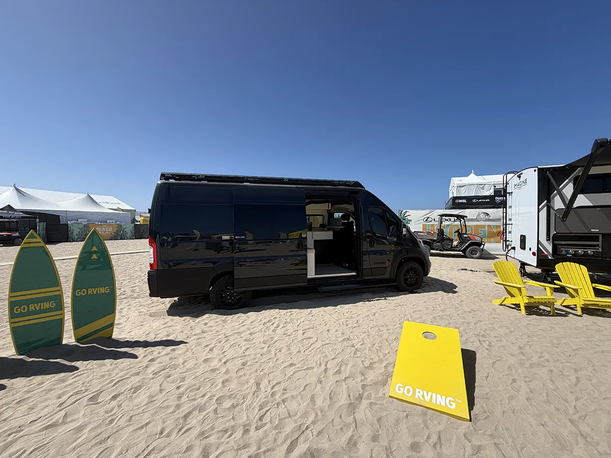A DM Vans LV7 camper van parked on the sand at the US Open of Surfing in Huntington Beach, side door open beside the GO RVing display boards