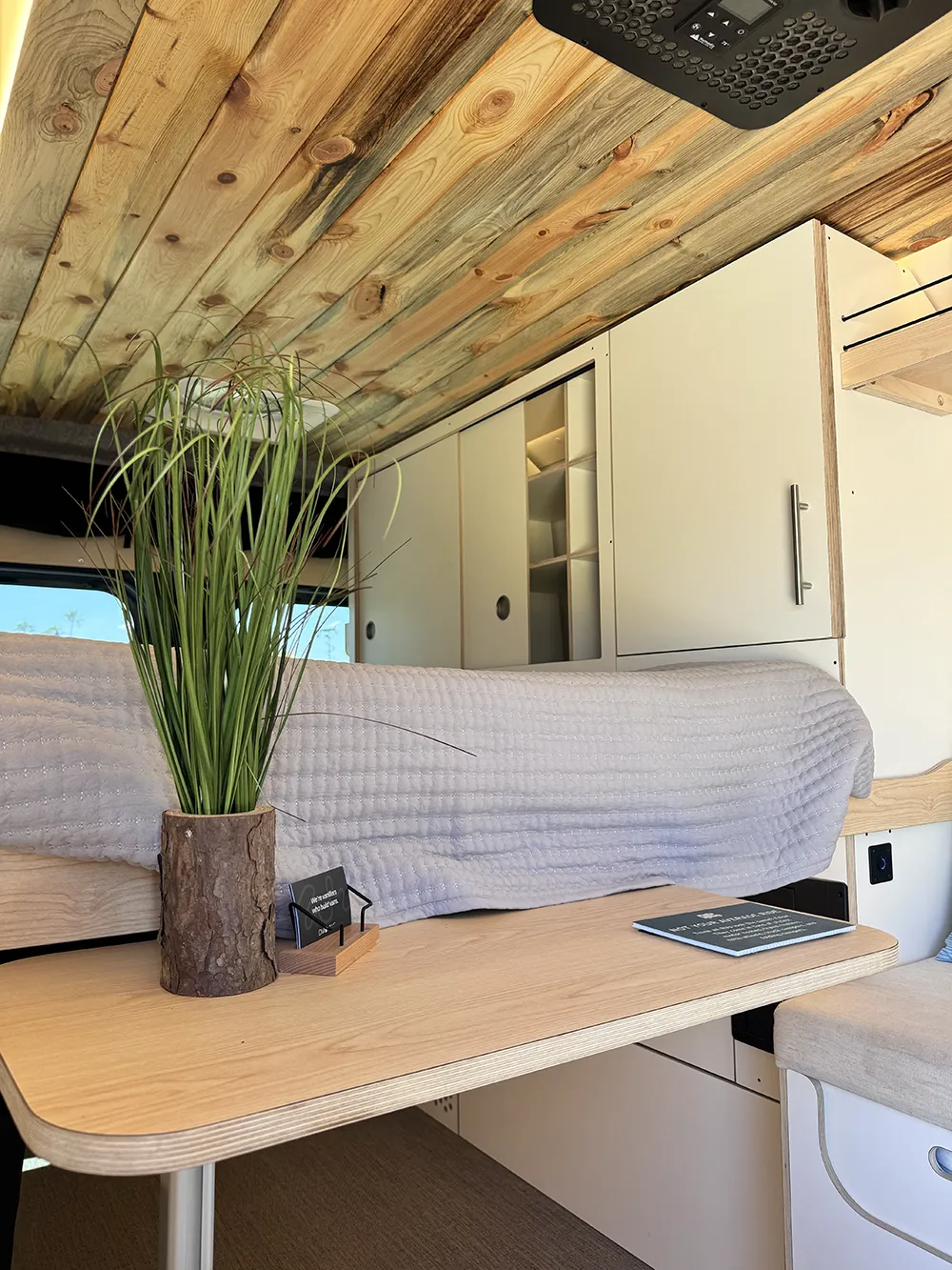 Inside a DM Vans camper van, showing the wood plank ceiling, the galley, upper cabinets, and the bed over the rear gearage