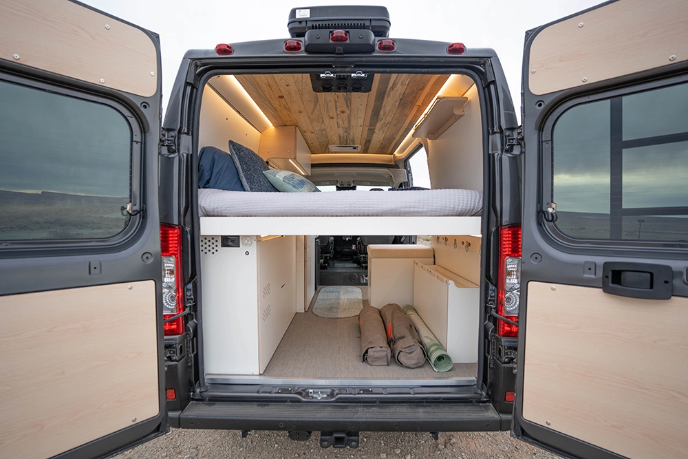 The rear doors of a DM Vans LV3 open, showing gear stowed in the gearage underneath the bed