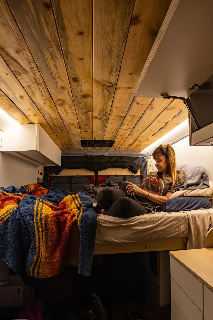 Woman relaxing on the camper van bed under the wood plank ceiling